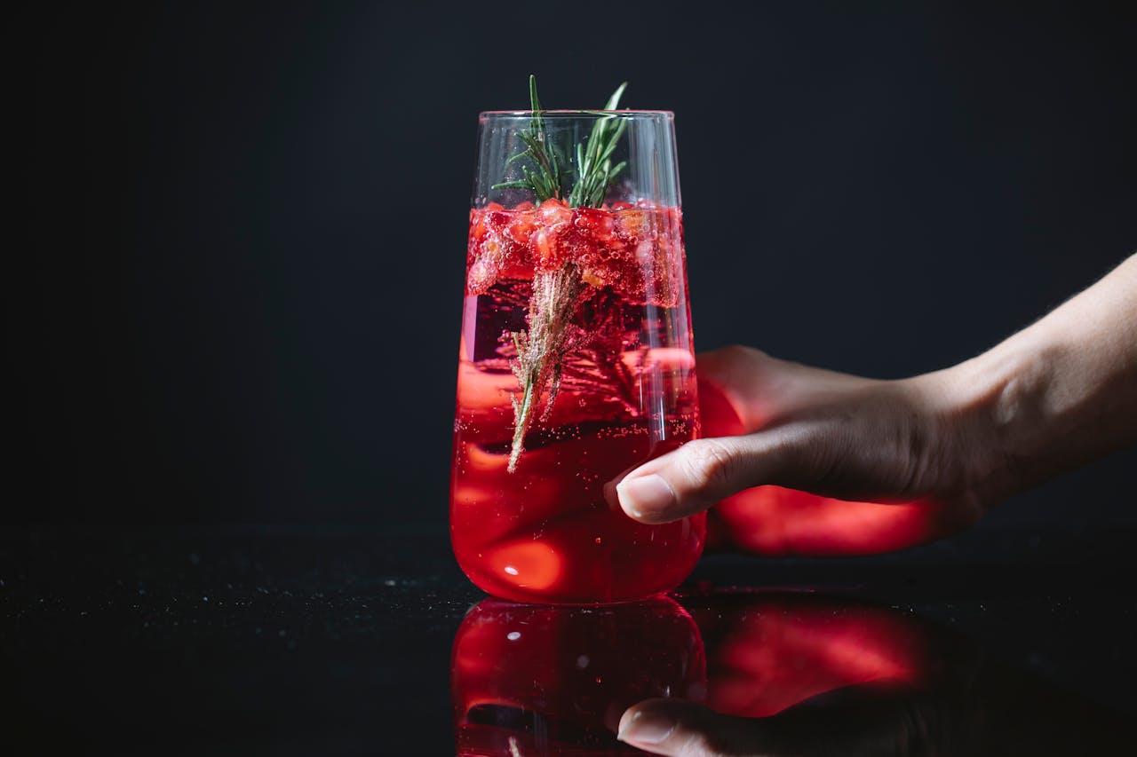 A fresh and vibrant berry cocktail garnished with rosemary, served in a crystal clear glass.