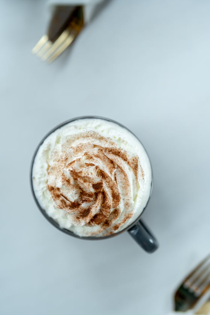 Top-down view of a latte with whipped cream and cinnamon in a ceramic mug on a table.