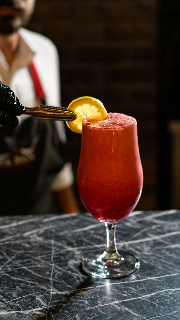 Vibrant red cocktail with lemon slice garnish on a marble bar, perfect for a stylish night out.