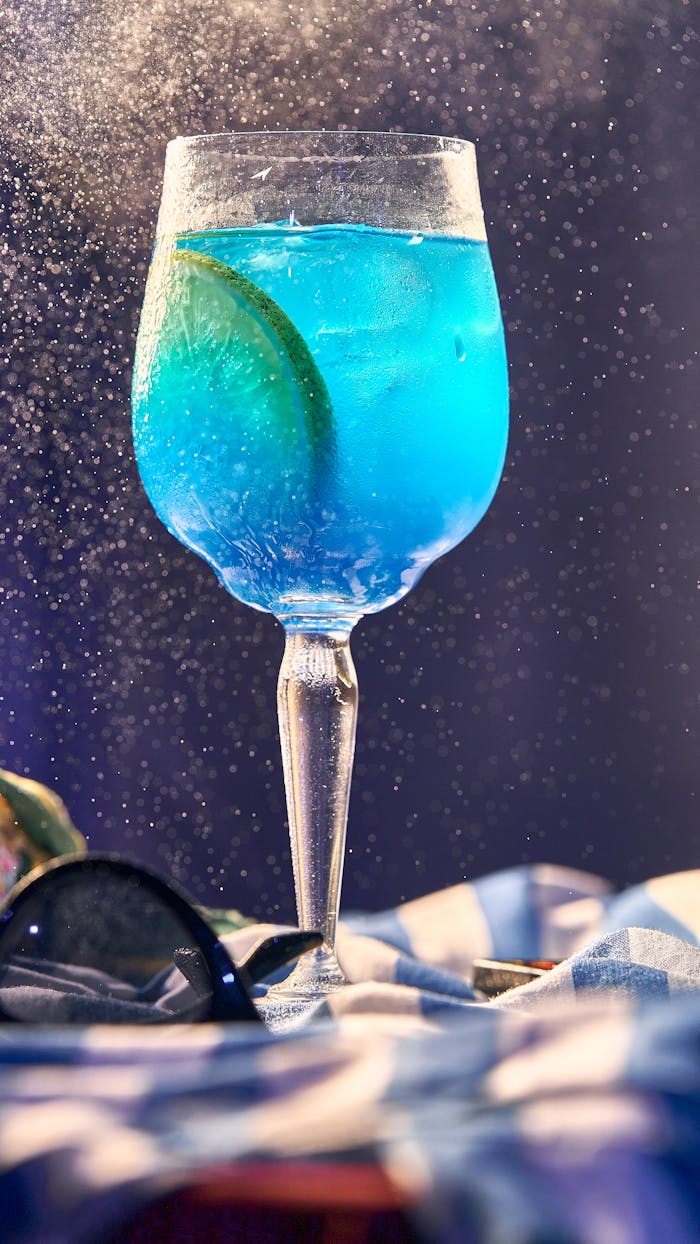 Close-up of a refreshing blue cocktail with lime in a glass, sprinkled with mist on a colorful table.